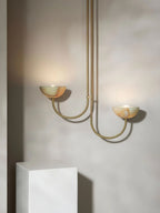 The Clérachic Lunaris pendant in brass, both bowls lit against a warm plaster wall.