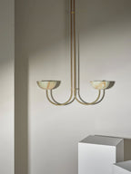 Clérachic Lunaris pendant in brass shown small in frame beside a white display plinth.