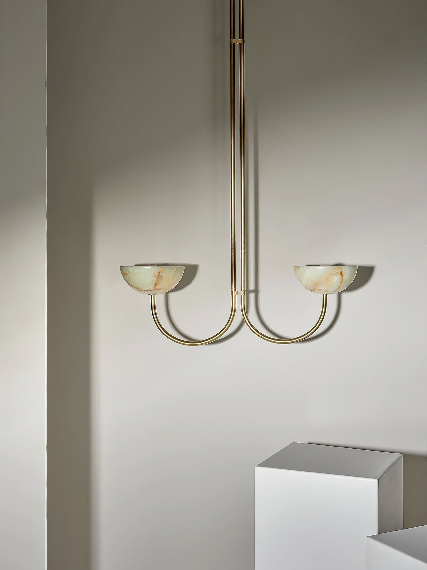 Clérachic Lunaris pendant in brass shown small in frame beside a white display plinth.