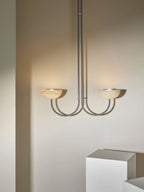 The Clérachic Lunaris pendant in nickel, twin bowls lit warm above a white plinth.