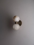 The Clérachic Lush Twin Globe Wall Sconce unlit on a pale plaster wall, its bronze arm and stacked alabaster globes reading as a quiet detail.
