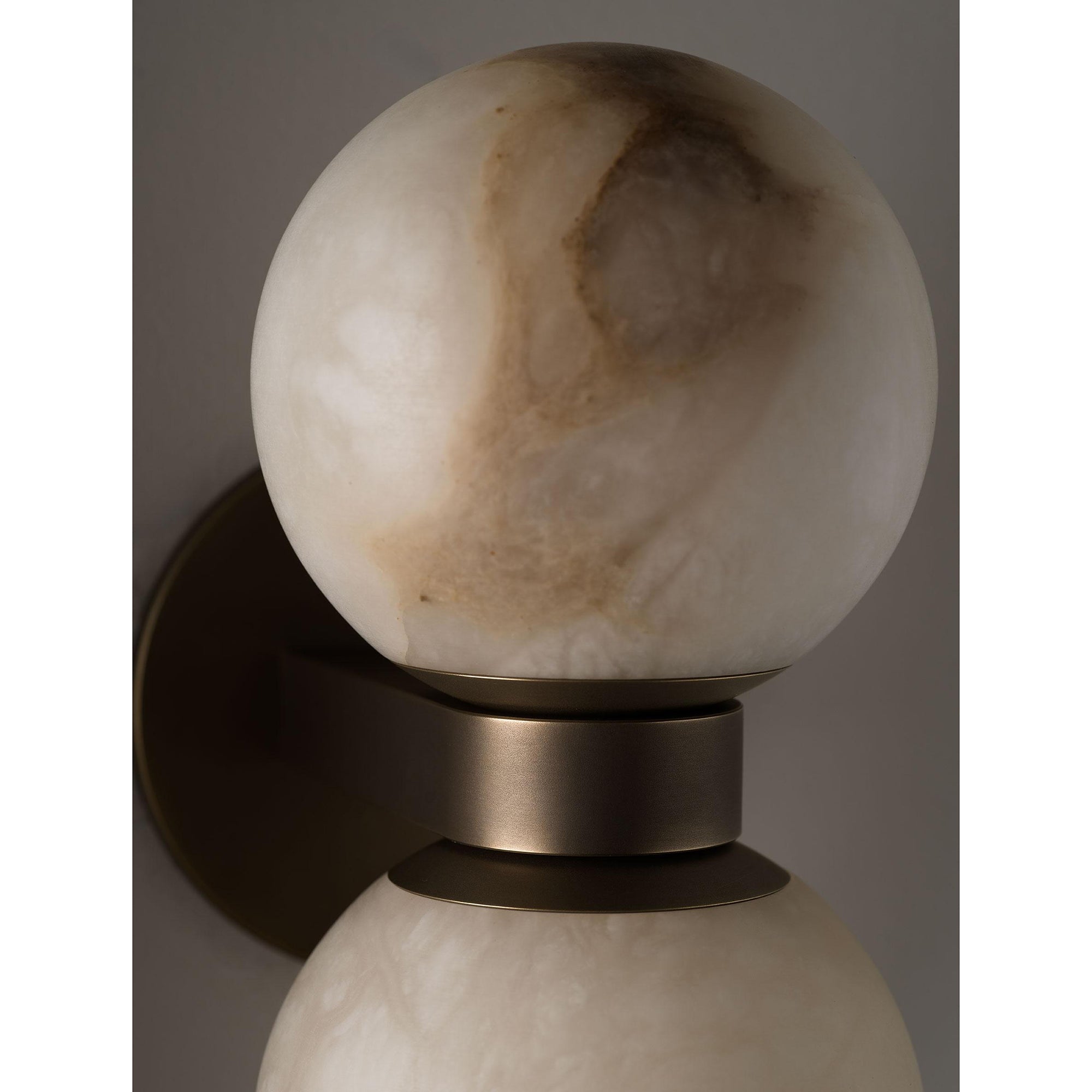 Close view of a Clérachic Lush Twin Globe Wall Sconce globe, the alabaster's amber veining and the machined bronze collar beneath it.