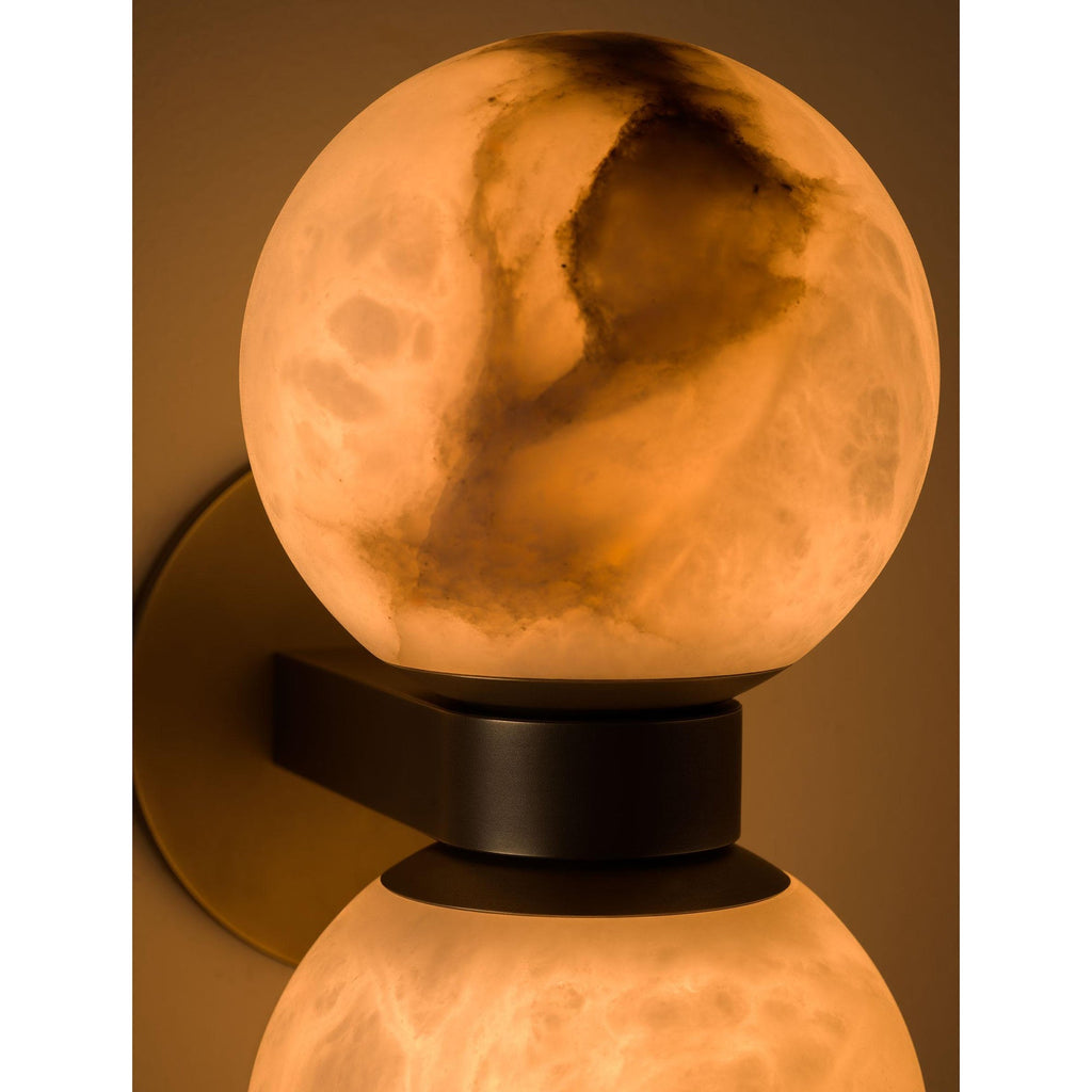 The upper alabaster globe of the Clérachic Lush Twin Globe Wall Sconce lit from within, warm light bringing the stone's veining forward.