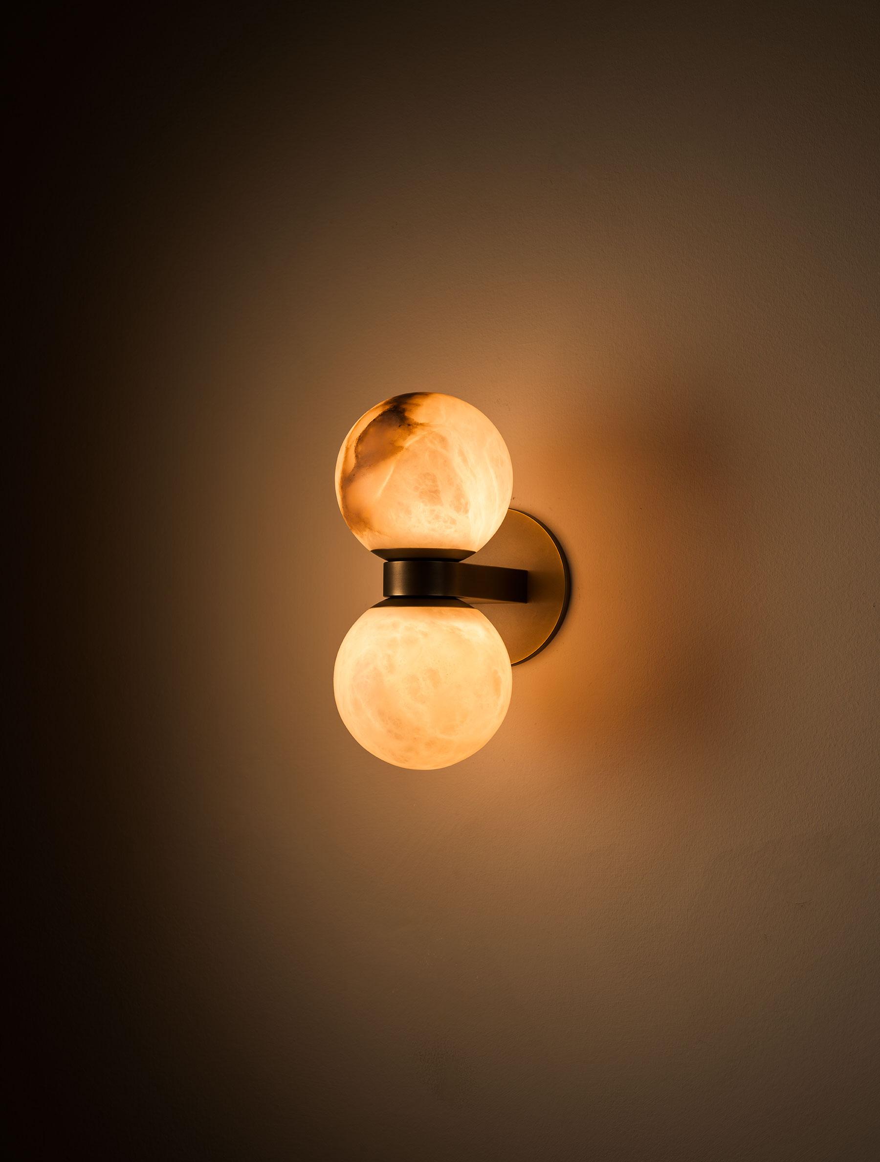 The Clérachic Lush Twin Globe Wall Sconce lit in a dark room, throwing a soft pool of warm light up and down the wall around it.