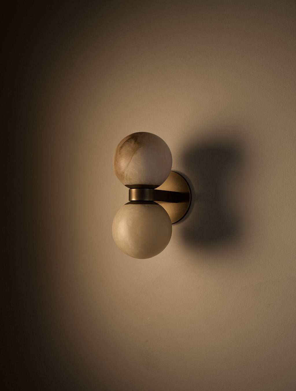 Angled view of the Clérachic Lush Twin Globe Wall Sconce on a warm wall, its bronze bracket casting a soft double shadow beside it.
