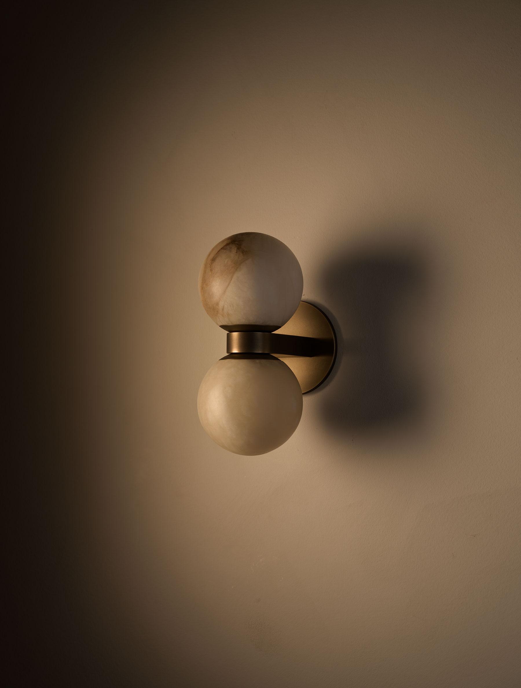 Angled view of the Clérachic Lush Twin Globe Wall Sconce on a warm wall, its bronze bracket casting a soft double shadow beside it.