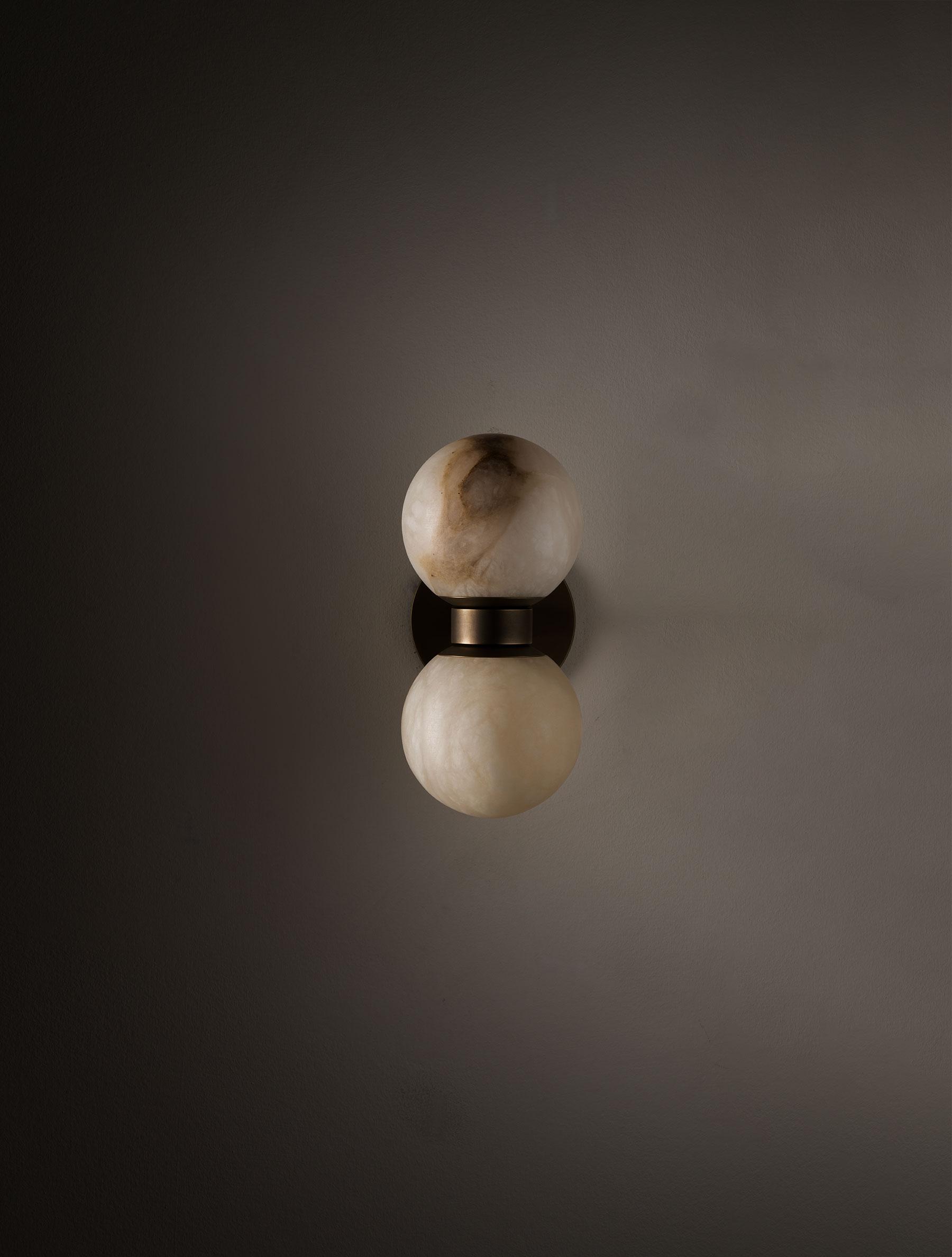 The Clérachic Lush Twin Globe Wall Sconce switched off against a dark grey wall, the bronze collar sitting between two pale stone globes.