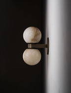 Profile of the Clérachic Lush Twin Globe Wall Sconce against a white corner wall, the flat bronze arm holding both globes clear of the plaster.