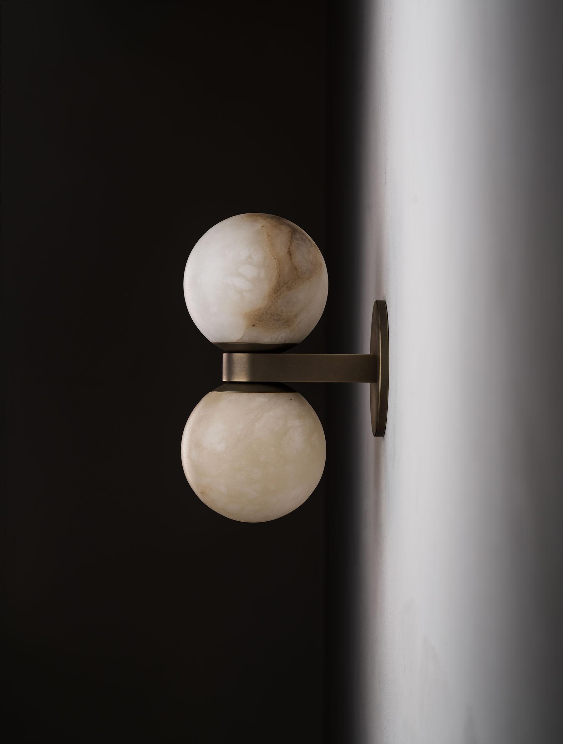 Profile of the Clérachic Lush Twin Globe Wall Sconce against a white corner wall, the flat bronze arm holding both globes clear of the plaster.