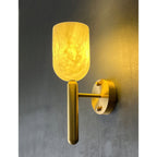 Clérachic Lyphaia alabaster sconce switched on, spilling a soft pool of warm light across the textured grey wall beside it.