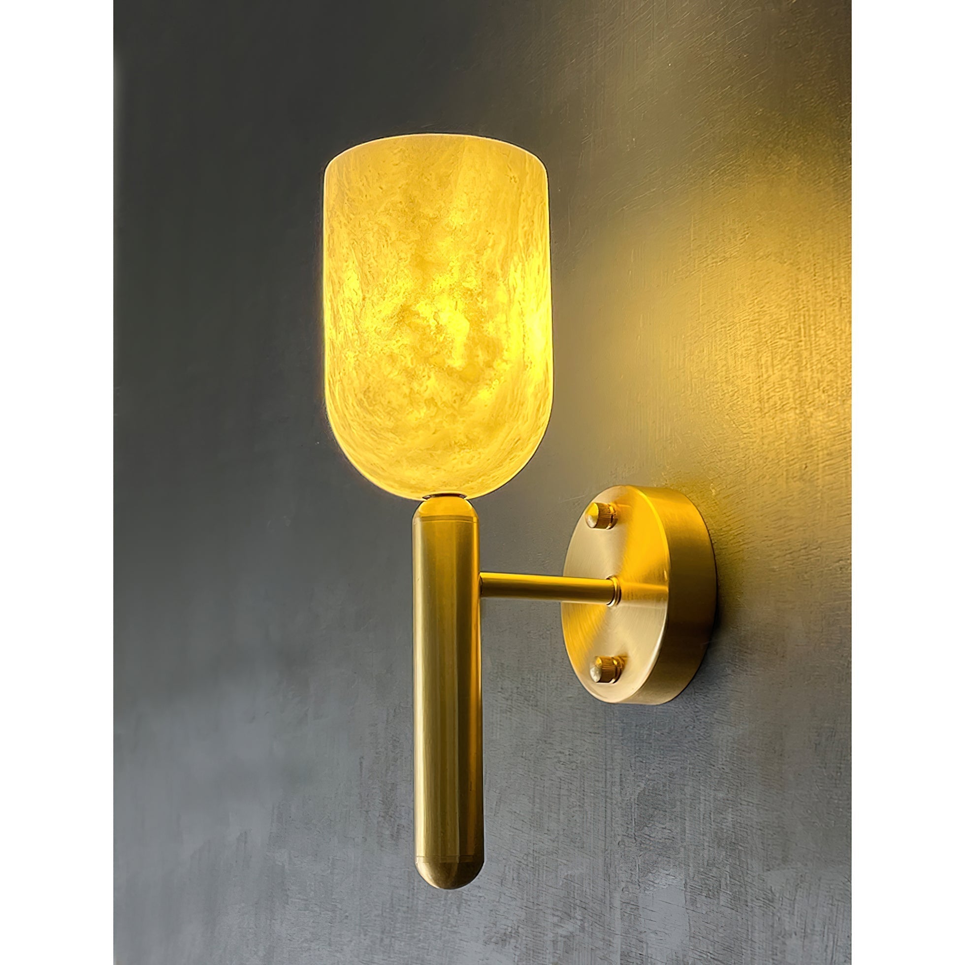 Clérachic Lyphaia alabaster sconce switched on, spilling a soft pool of warm light across the textured grey wall beside it.