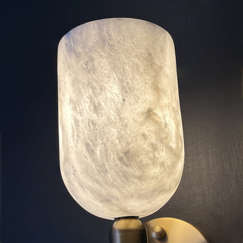 Close-up of the glowing alabaster cup on the Clérachic Lyphaia wall sconce, its clouded grain lit from within above the brass collar.