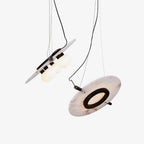 Two Clérachic Magma pendants on white, one tilted to show the alabaster disc and its black ring.