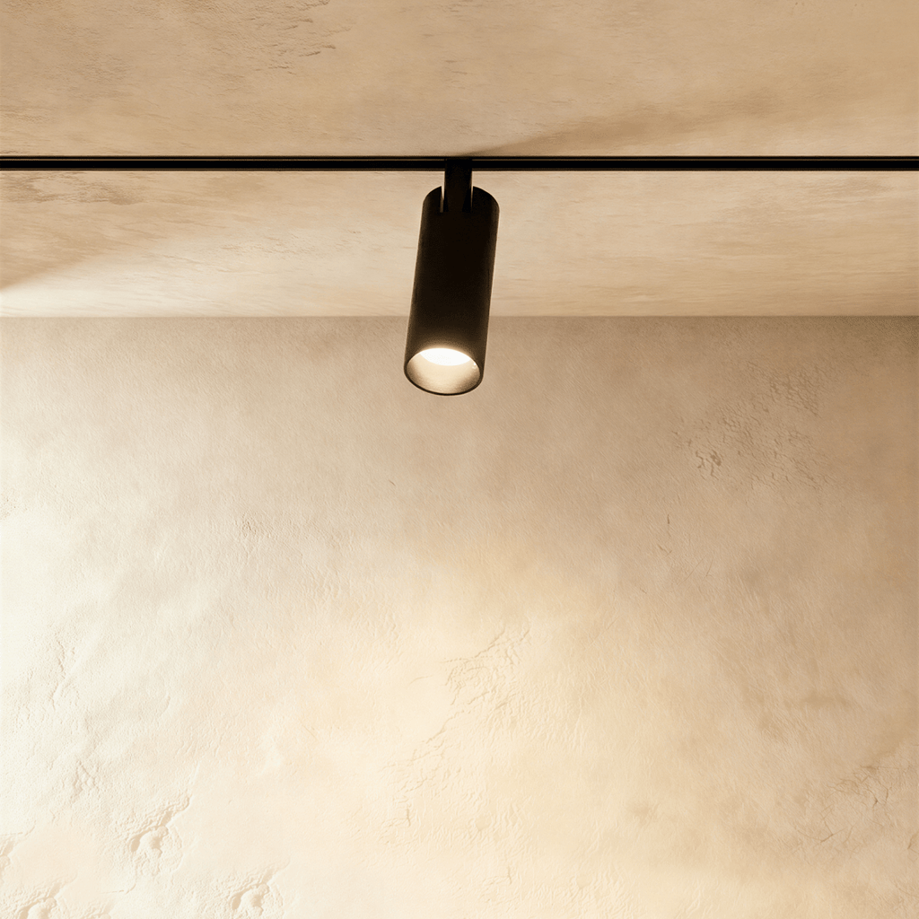 Clérachic track spotlight in black, its lit lens facing down over a limewashed plaster wall.