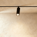 Clérachic track spotlight in black, its lit lens facing down over a limewashed plaster wall.