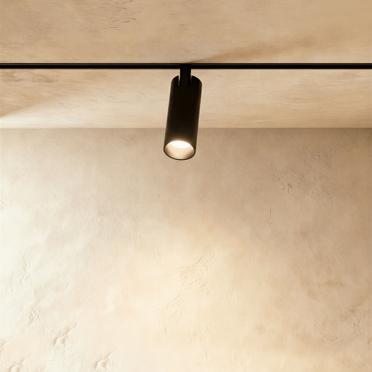 Clérachic track spotlight in black, its lit lens facing down over a limewashed plaster wall.