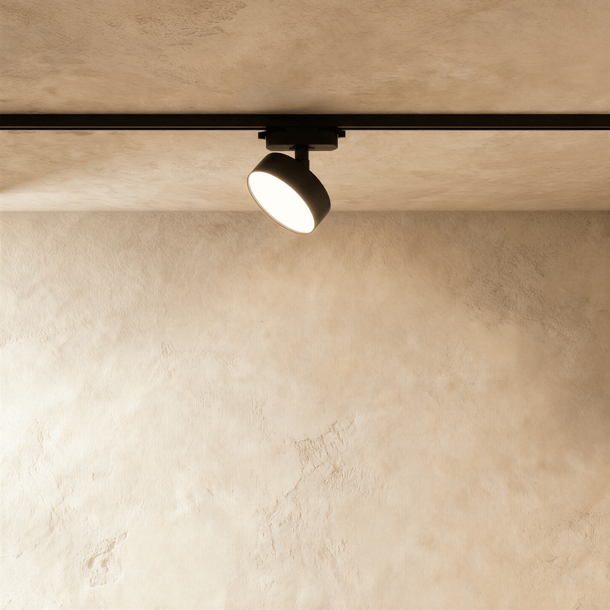 Clérachic black round track light head, angled on a black rail beneath a limewashed ceiling, its flat disc face glowing warmly.
