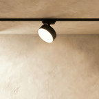 Clérachic larger black round track light head on a black rail, with a wide drum body and a glowing frosted disc face.