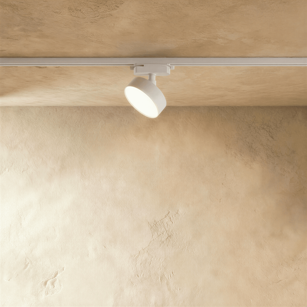 Clérachic white round track light head on a white rail against a warm plaster ceiling, its slim disc face softly lit.