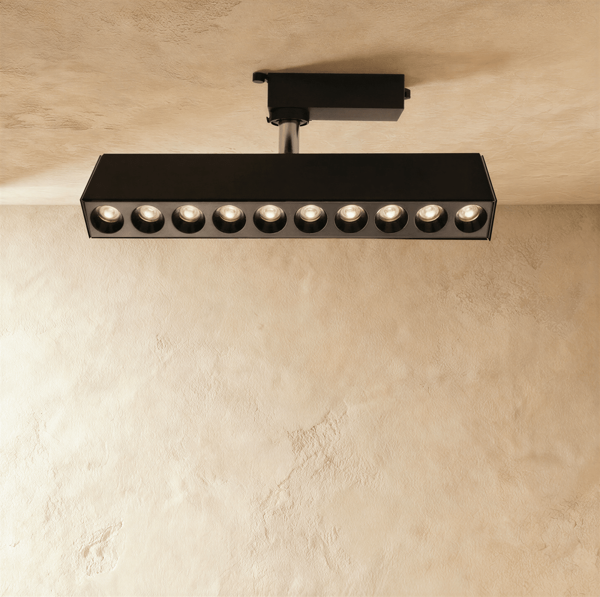 Clérachic long black ten-spot track spotlight bar with warm recessed lenses glowing, mounted on a track adaptor and stem.