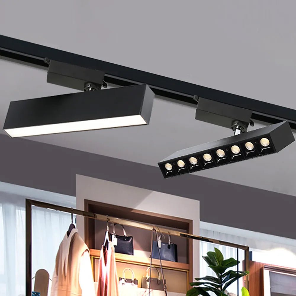 Clérachic black linear track light and an eight-spot track spotlight bar on a black rail above a clothing rail in a shop.