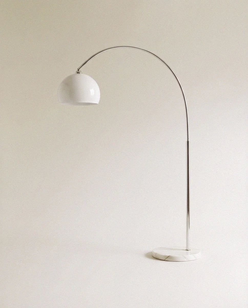 In white, this Clérachic floor lamp curves a slim chrome arm from a marble base to a glossy dome shade.