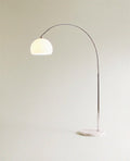 Lit from within, the white dome shade of this Clérachic floor lamp glows atop its curved chrome arm.