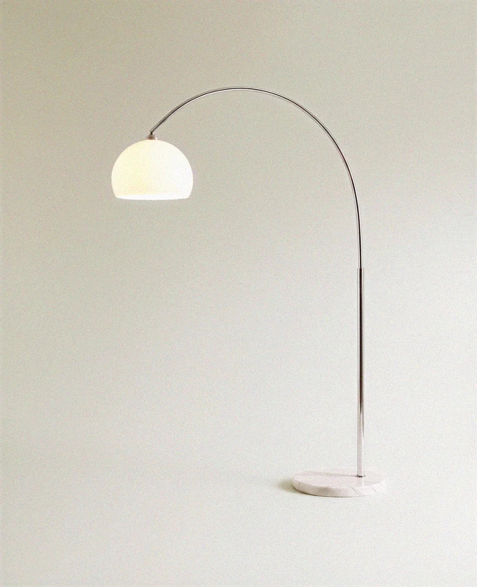 Lit from within, the white dome shade of this Clérachic floor lamp glows atop its curved chrome arm.