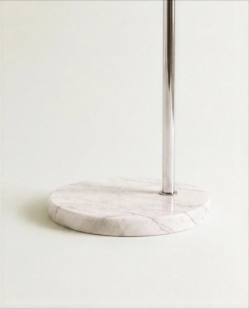 A close view of the Clérachic floor lamp's round white marble base, where the polished chrome pole meets the stone.