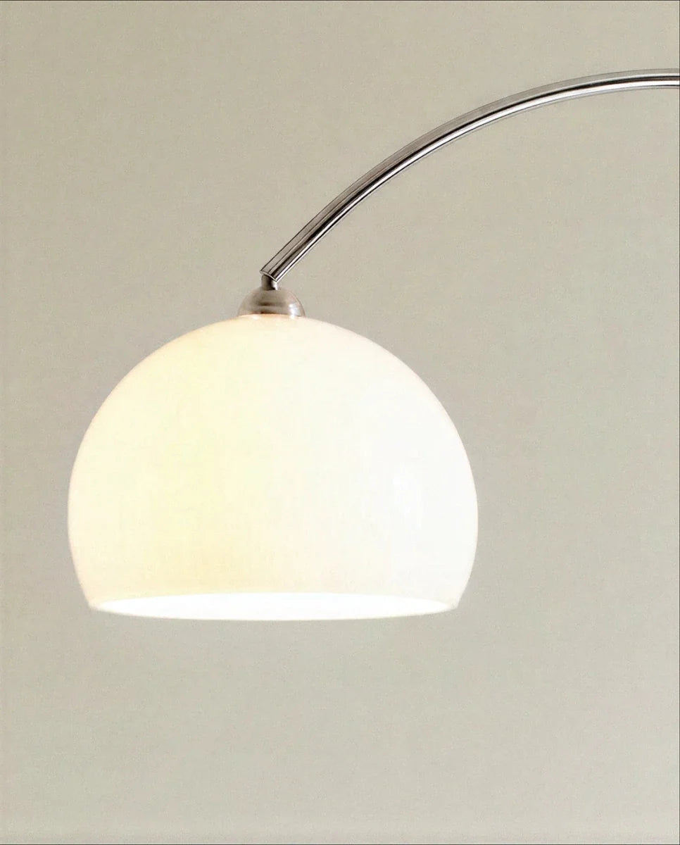 This close-up shows the Clérachic floor lamp's white dome shade glowing softly at the end of its chrome arc.