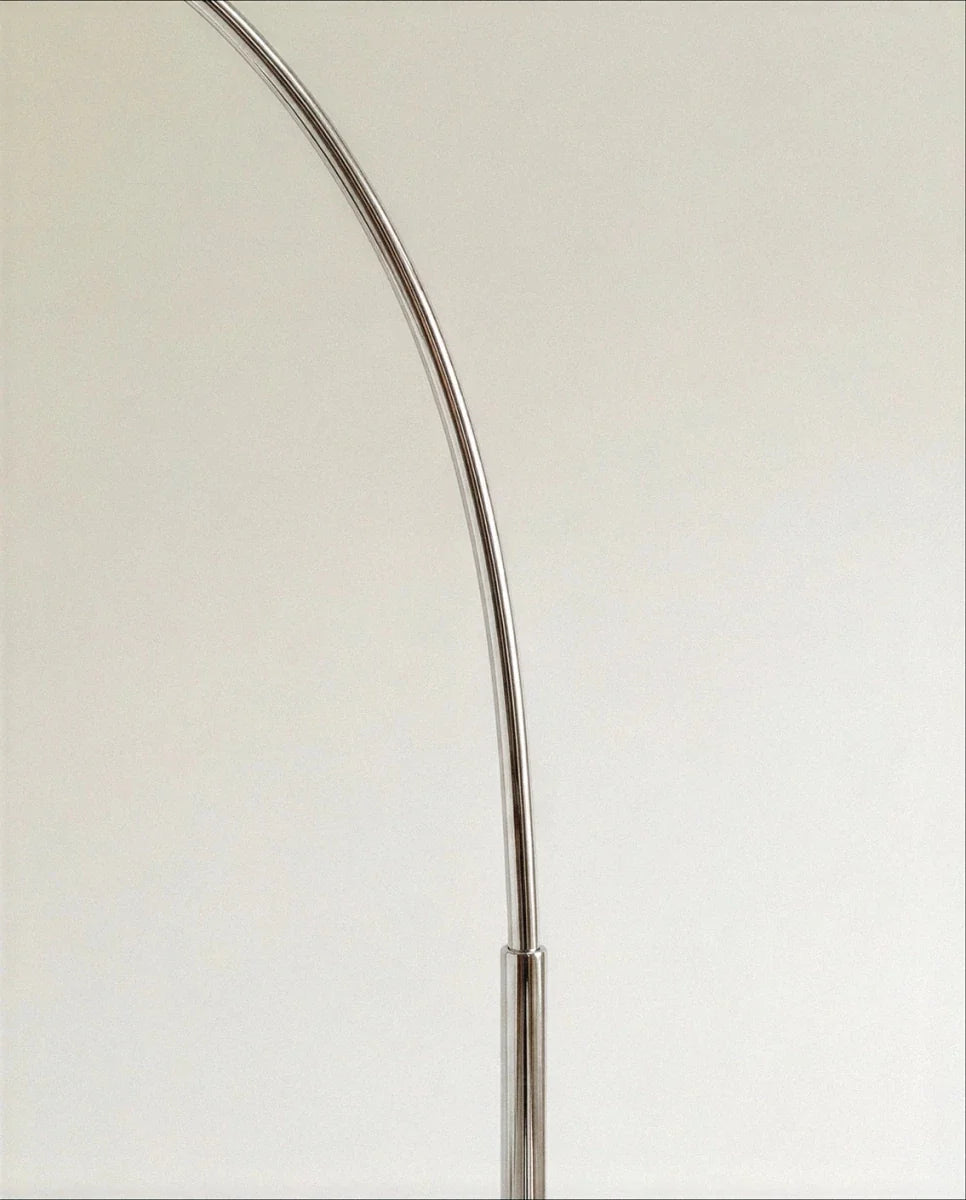 A detail of the Clérachic floor lamp's polished chrome arc, curving smoothly from its slender upright pole.