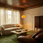 In a warm living room with a boucle sofa, this orange-shaded Clérachic floor lamp arcs gently over a marble coffee table.