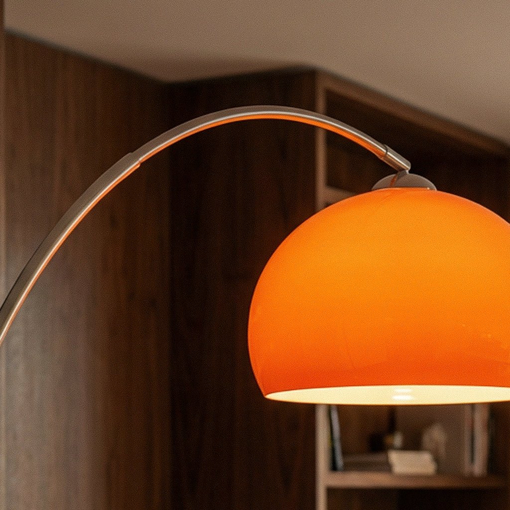 A close-up of the glossy orange dome shade on this Clérachic floor lamp, glowing warmly against a wood-panelled room.