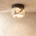Clérachic ceiling light: a veined marble drum on a black metal mount, lit from within, fixed to a limewashed ceiling.
