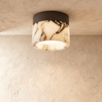 Clérachic ceiling light: a veined marble drum on a black metal mount, lit from within, fixed to a limewashed ceiling.