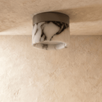Clérachic unlit marble drum ceiling light with dark natural veining on a black metal mount, against a plaster ceiling.