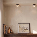 Two Clérachic marble drum ceiling lights above a shelf holding books, a brass figure and a framed ink drawing.
