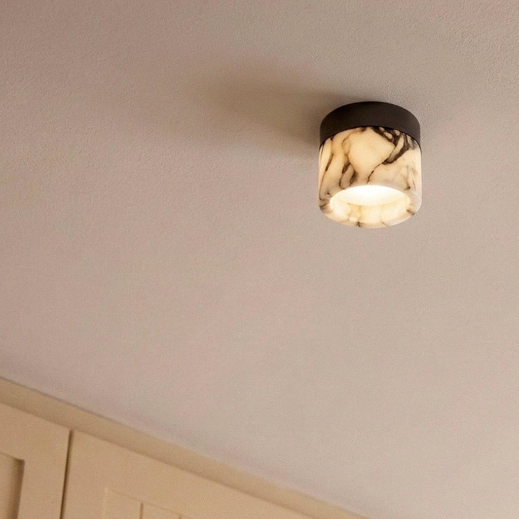 Close view of a Clérachic marble drum ceiling light with a black mount, glowing warmly on a pale ceiling above cabinets.