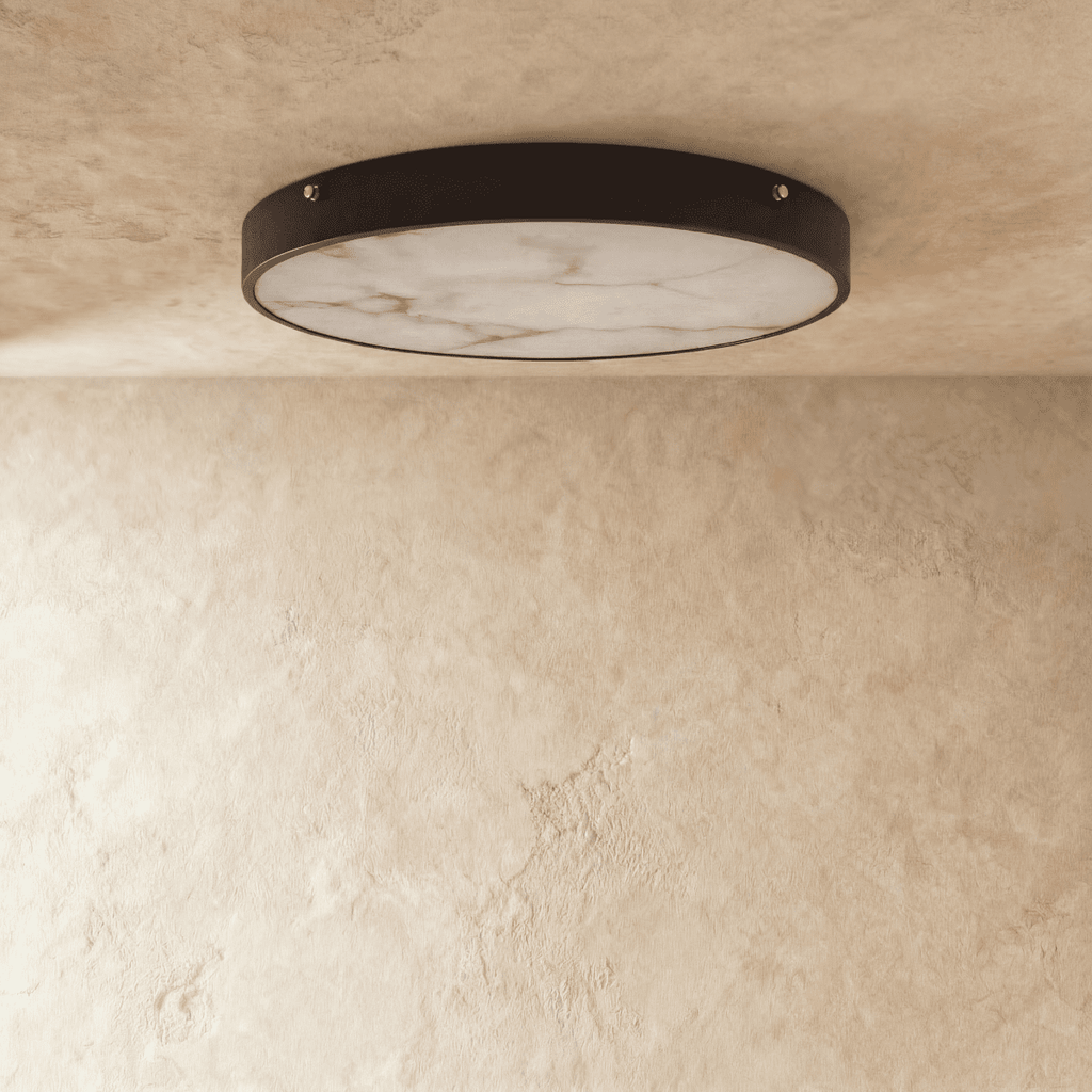 Clérachic flush-mount ceiling light with a veined marble diffuser in a slim dark metal rim, shown on a limewash ceiling.