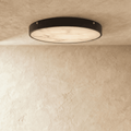 Clérachic round flush ceiling light, lit, with soft marble veining across the diffuser inside a thin dark rim.