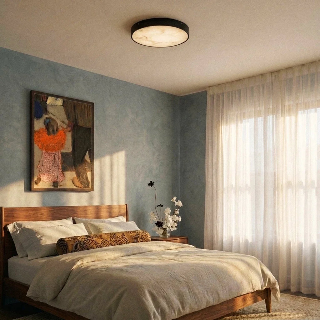 Clérachic round marble-diffuser ceiling light above a walnut bed in a bedroom with a blue wall and sheer curtains.