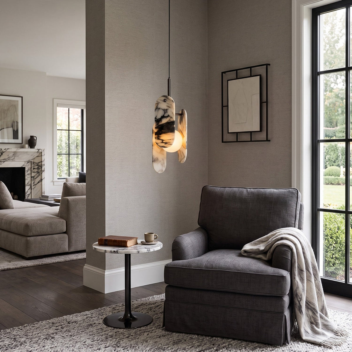 A Clérachic marble pendant lights a reading corner with a grey armchair, a round side table and a tall black-framed window.