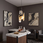 A Clérachic marble pendant hangs over a marble-topped bar with a drinks tray, between two framed marbled artworks.