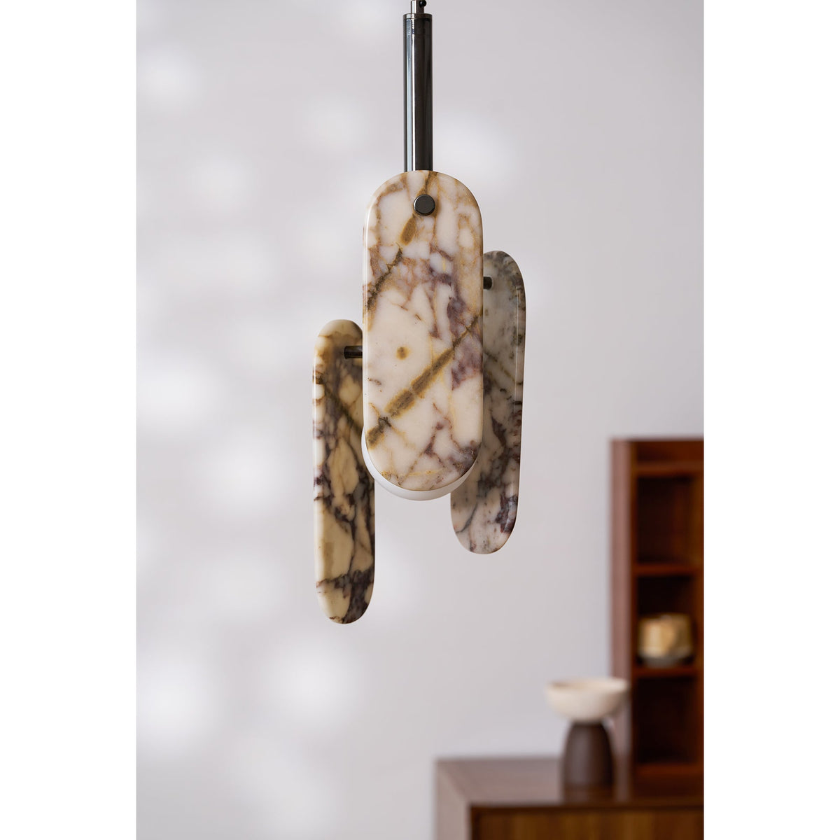 A Clérachic pendant with cream marble panels veined in violet and amber hangs in front of a pale wall and a wooden cabinet.