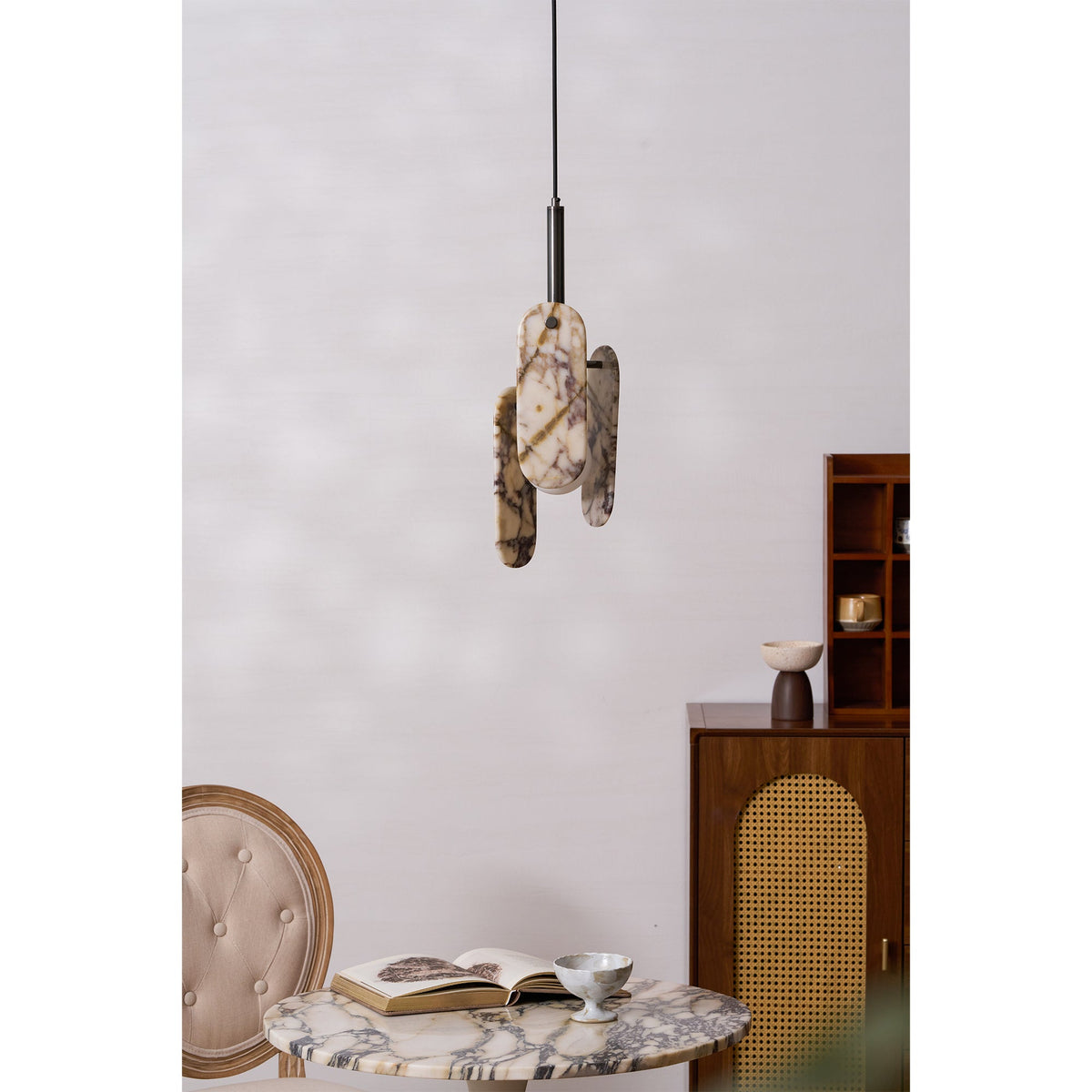 A Clérachic pendant with cream, violet-veined marble panels hangs above a round marble table with an open book and a velvet chair.