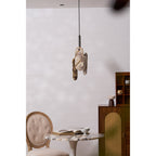 A small Clérachic marble pendant hangs above a round marble-topped table and a tufted chair, beside a rattan-fronted cabinet.