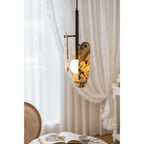 Warm light glows through the cream marble panels of this Clérachic pendant, with a sheer curtain and a table behind it.