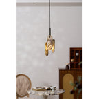 A Clérachic pendant with cream marble panels glows above a marble-topped table, a book and a tufted chair beside a wooden cabinet.