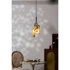 A lit Clérachic pendant with cream marble panels throws speckled light on the wall above a marble table and a tufted chair.