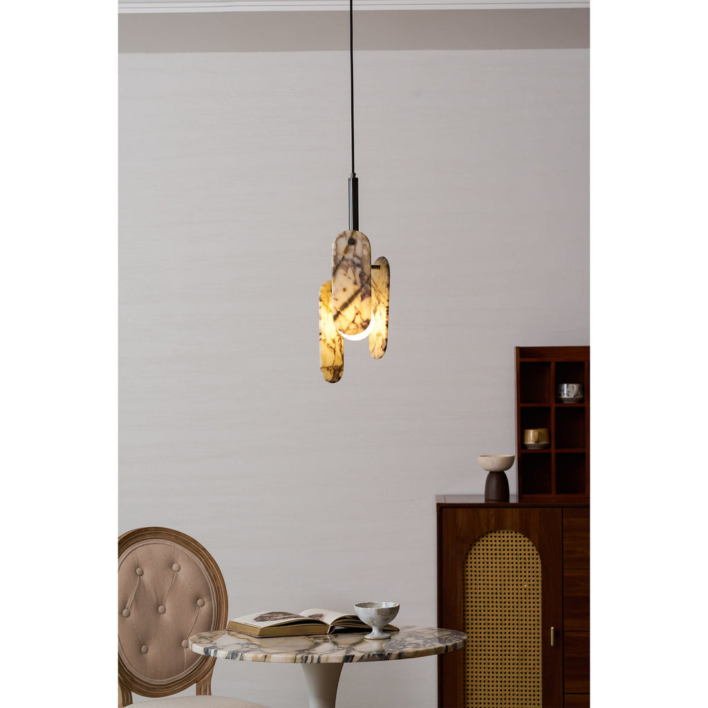 A Clérachic marble pendant glows amber above a round marble table, with an open book, a small cup and a wooden cabinet beside it.